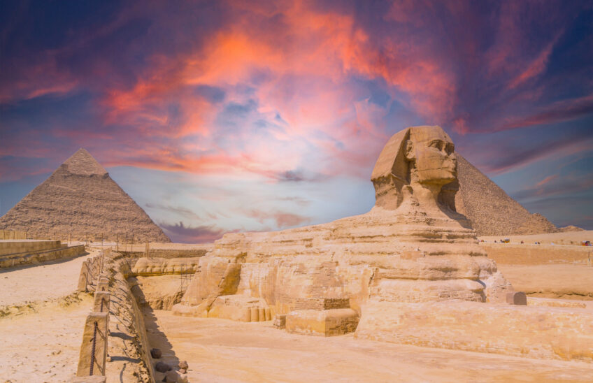 View of the the Great Sphinx and the Pyramids of Giza against a colorful sunset in Giza, Egypt